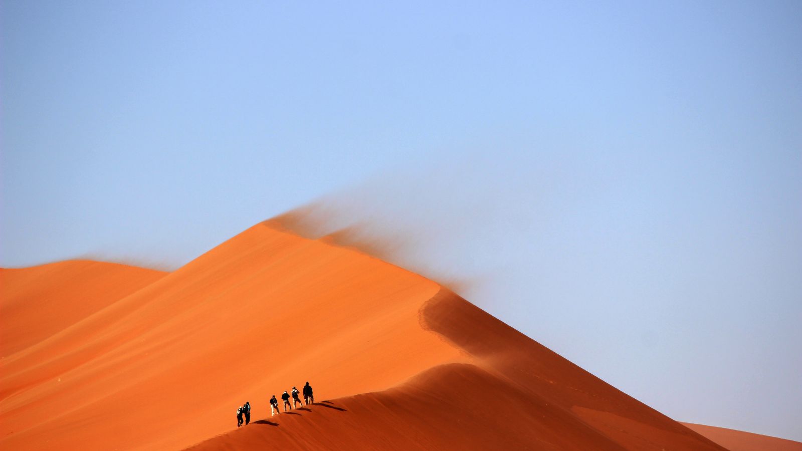 People walking up an orange sand dune